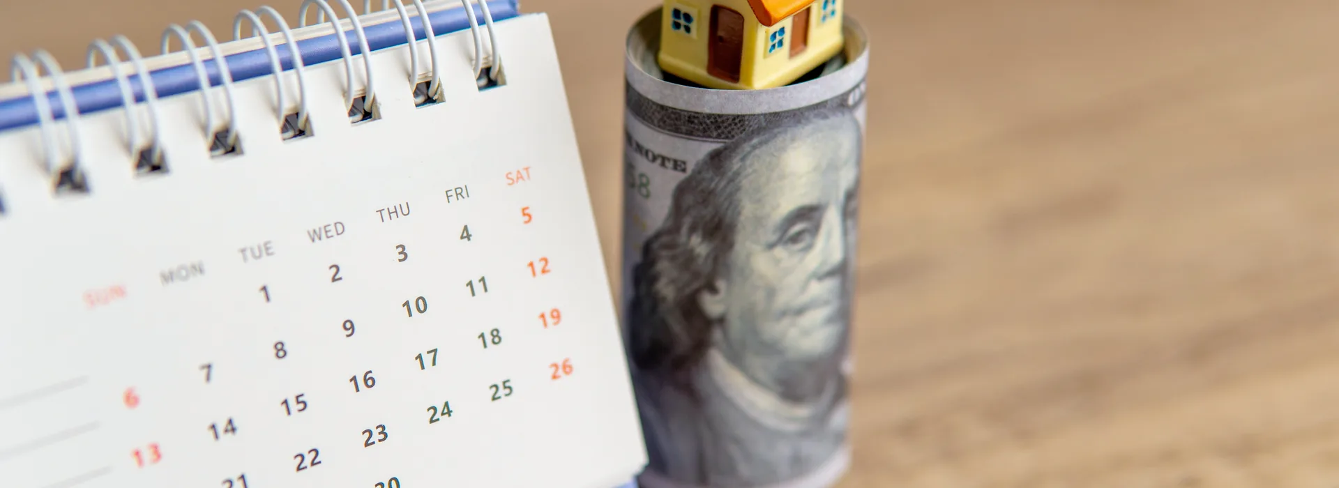 Calendar, rolled cash, and a house model representing a deferred payment