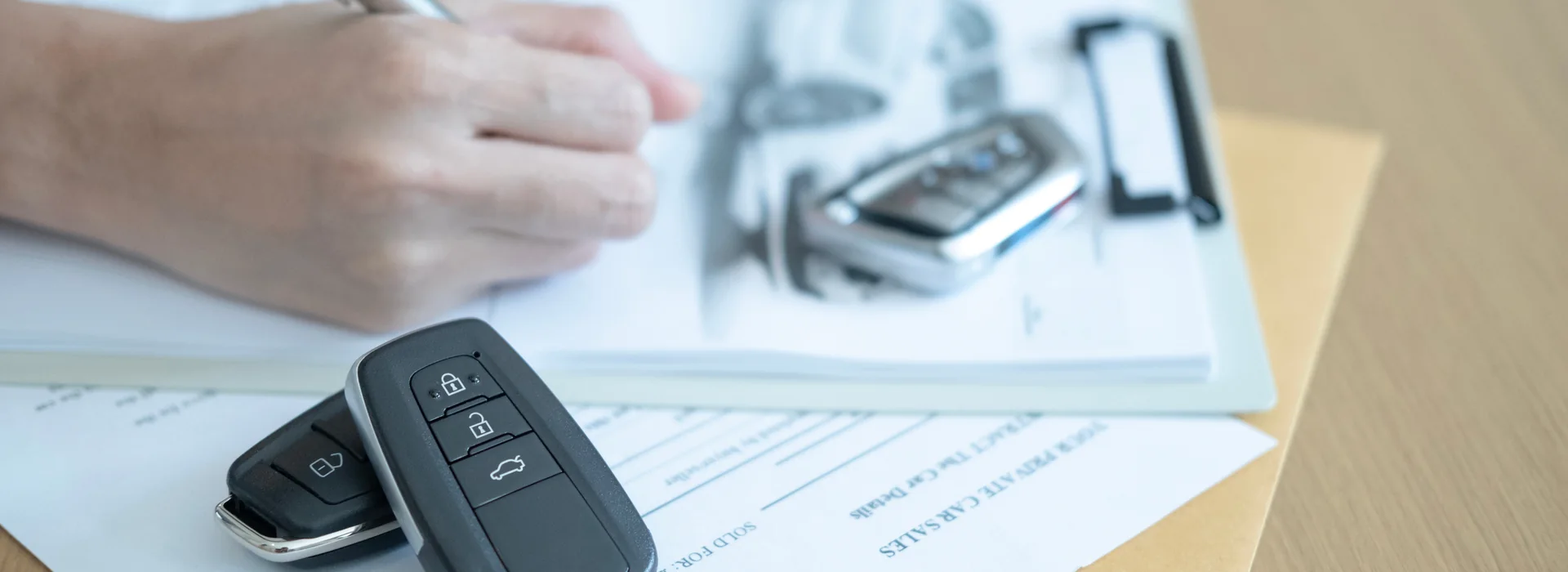 Hand signing vehicle title paperwork beside car keys