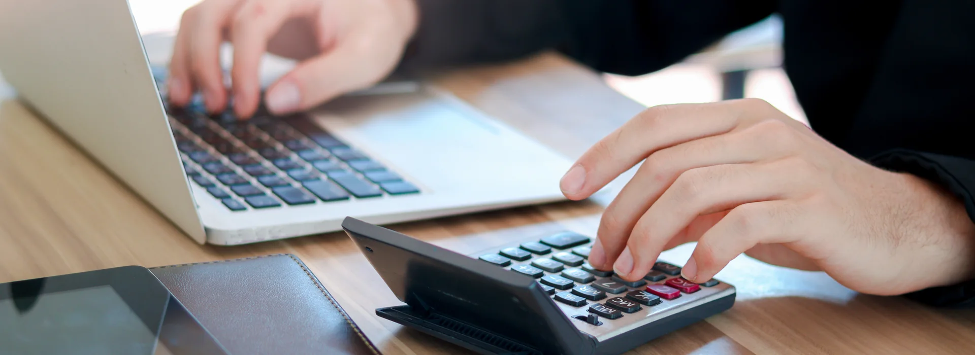 Person comparing interest rates and loan costs with a calculator and laptop
