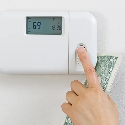 Hand adjusting a home thermostat beside U.S. dollars