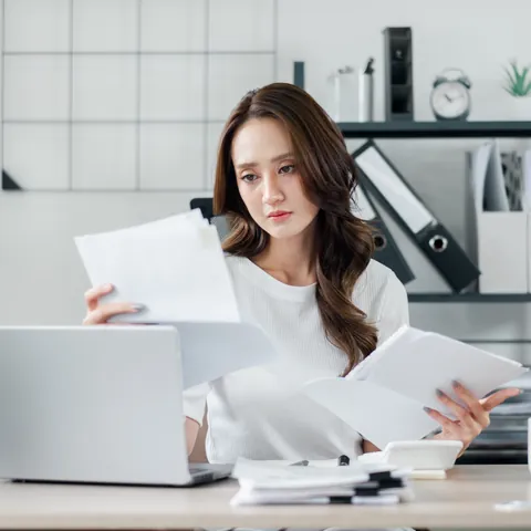 Self-employed woman organizing multiple financial documents at her workspace