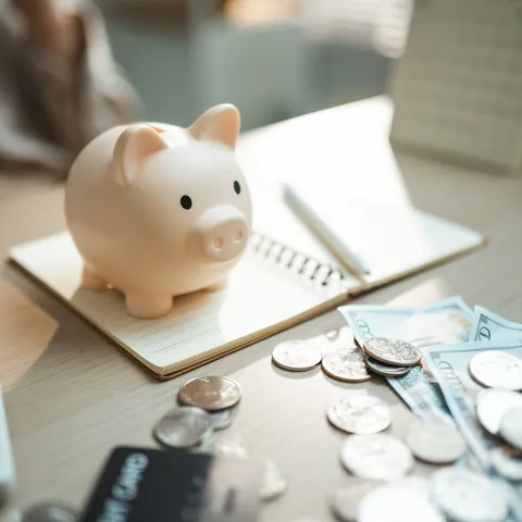 Piggy bank with cash, coins, calculator, and notebook on desk