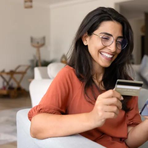 Woman holding a debit card while using a smartphone at home