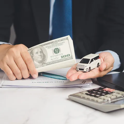 Borrower holding cash and a toy car above title loan paperwork