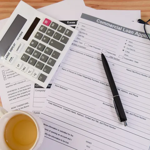 Loan application paperwork with a calculator, pen, and glasses