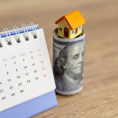 Calendar, rolled cash, and a house model representing a deferred payment