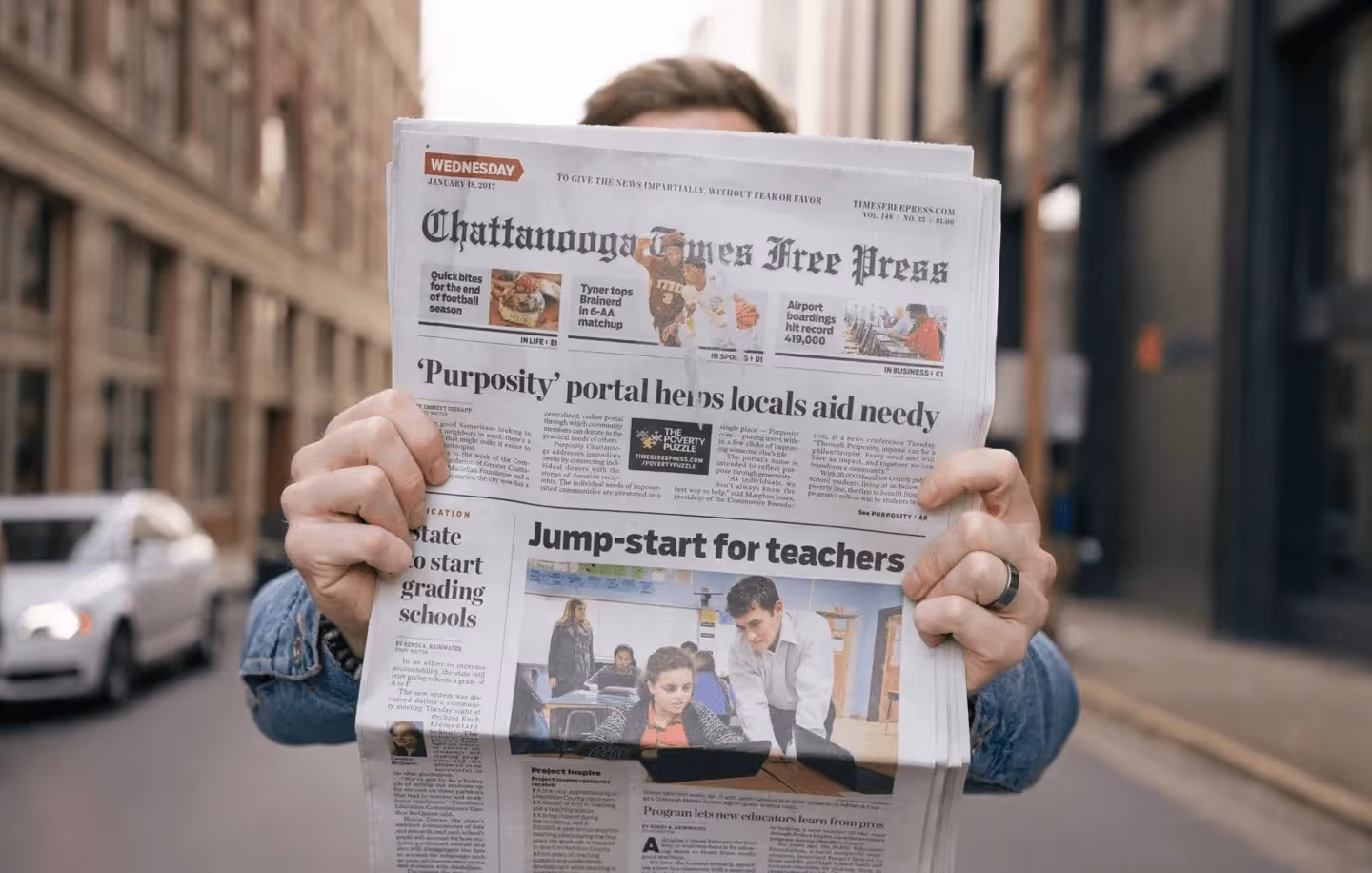 A man holds up a newspaper with a headline about Purposity