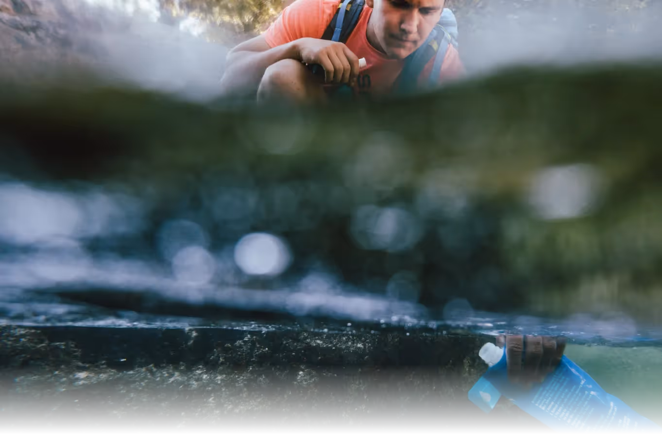 An underwater image of a hiker filling a Sawyer filter.