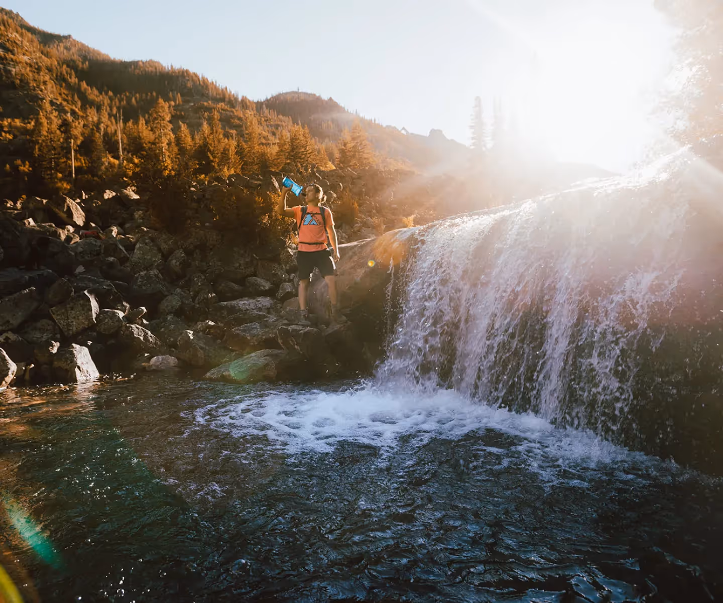 A hiker drinks from a Sawyer water bottle, filled from a small water rapid.