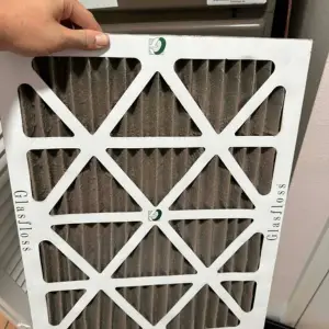 hand holding dirty air filter in front of air conditioner unit