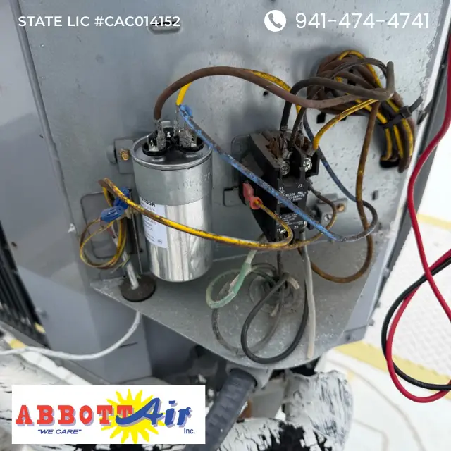 Close-up of an air conditioner capacitor and wiring inside a metal unit with Abbott Air logo and contact info.