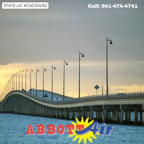 Long bridge with street lamps stretching over calm water under a cloudy sky at sunset, with the Abbott Air company logo and contact number 941-474-4741 displayed.