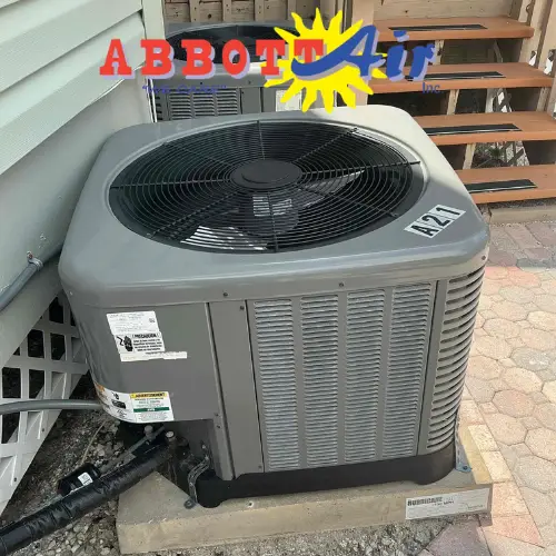 Outdoor air conditioning unit installed on a concrete pad next to a house, with an ABBOTT Air logo superimposed on the image.