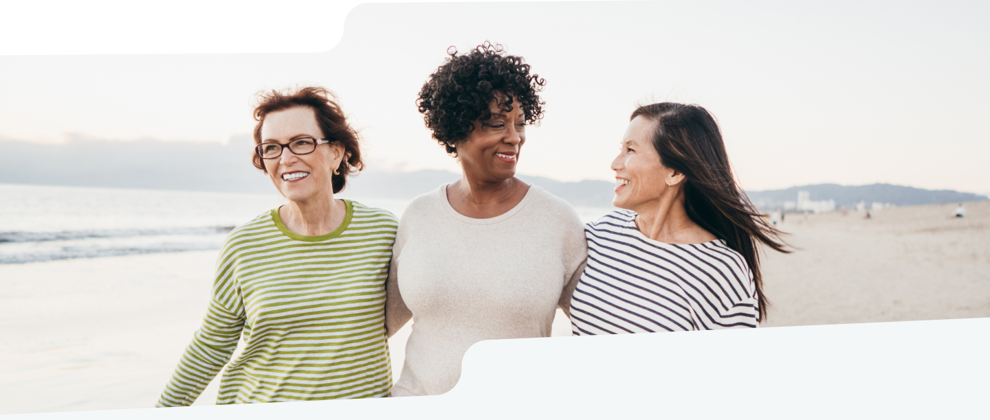 Photo of 3 middle-aged women smiling while walking along a beach.