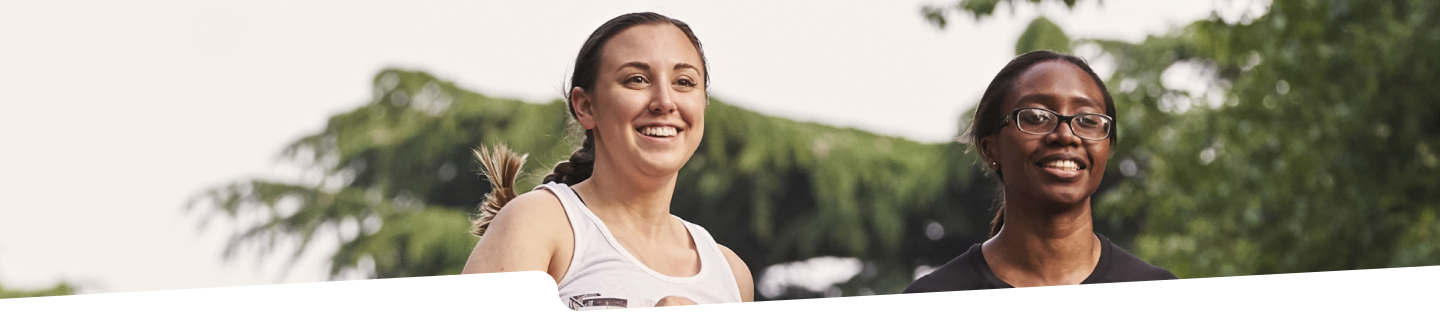 Photo of two women smiling while running through a park.