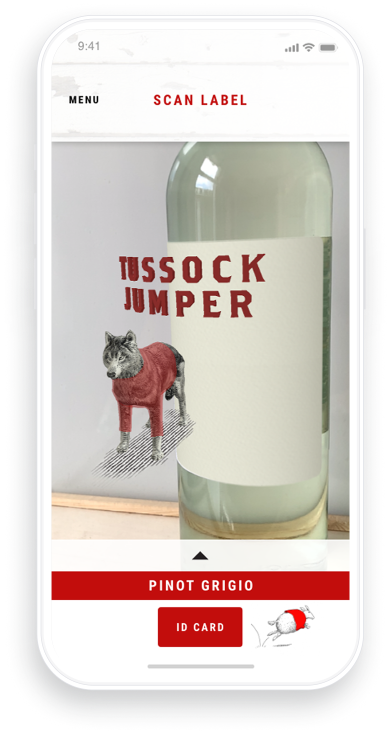 Mobile phone screen showing an app interface labeled Scan Label with a wine bottle image. The label reads 'Tussock Jumper' with an illustration of a wolf wearing a red sweater. Below the bottle image is a red button labeled 'ID Card' and 'Pinot Grigio' text above it.