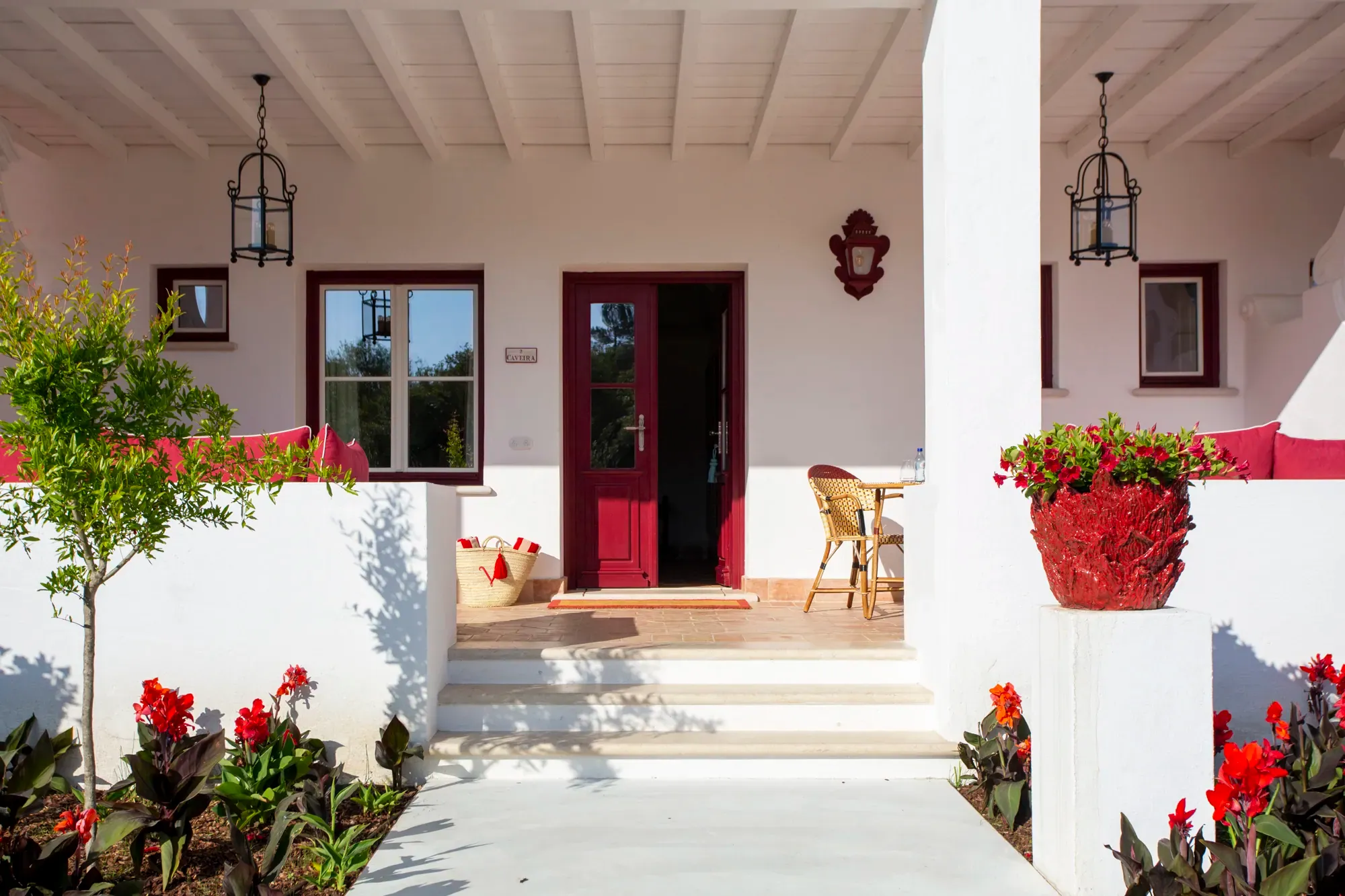 Terrace of a suite at Vermelho Melides, one of the best small hotels in Portugal, with red accents, a shaded sitting area, and vibrant flowers.