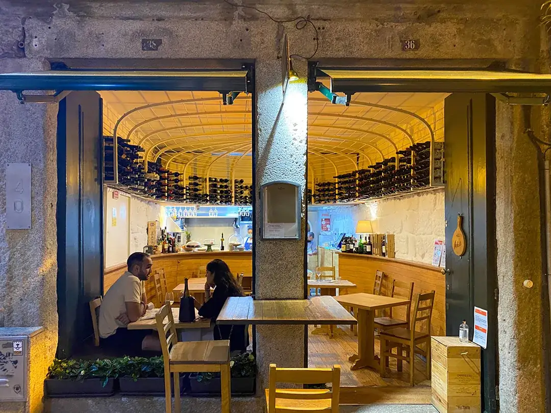 Inside Taberna dos Mercadores restaurant in Porto, showing open kitchen, dining tables and wine cellar above