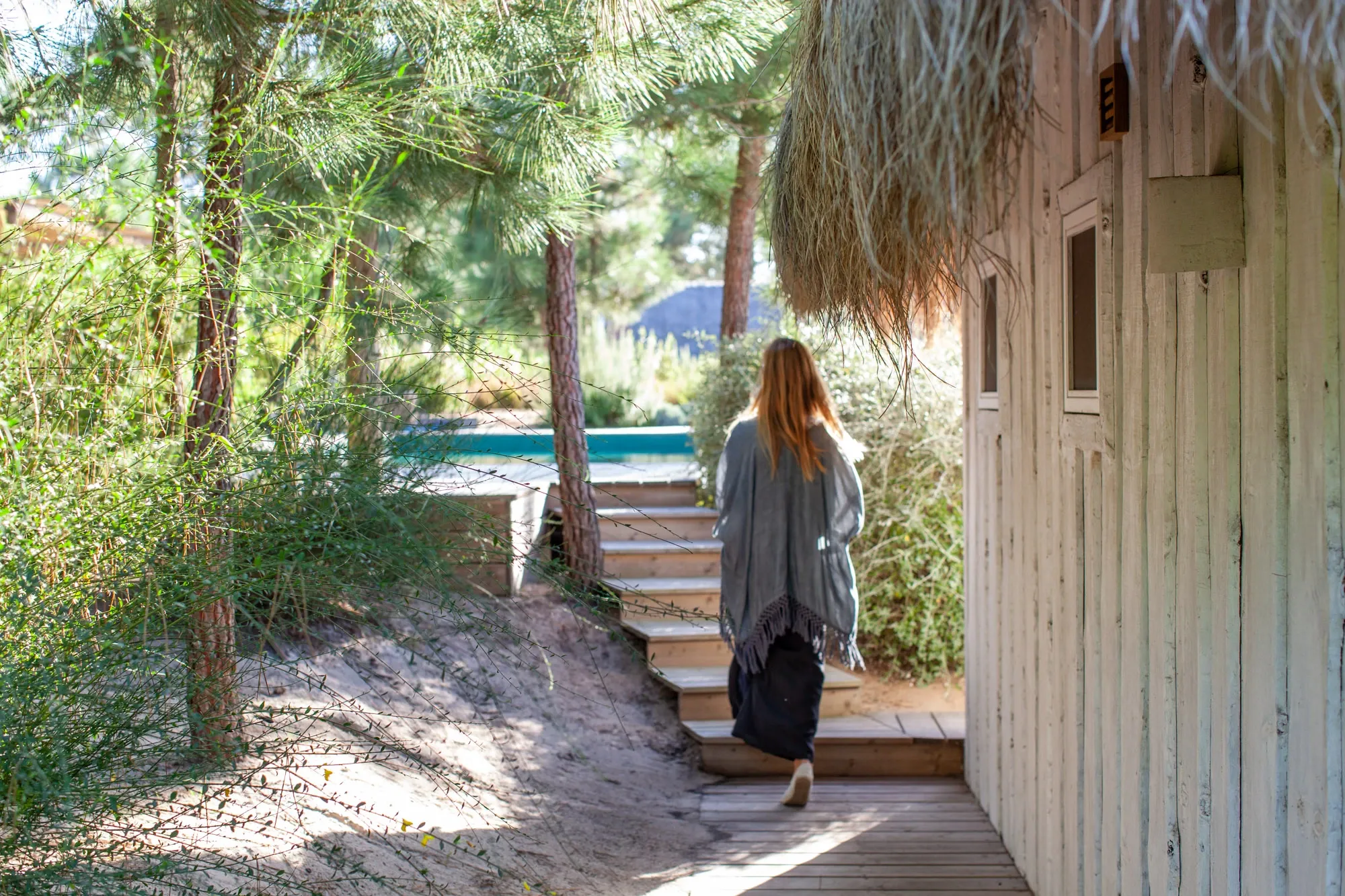 Natural wood cabin with thatched roof and turquoise pool surrounded by pine trees - insider guide Comporta Portugal.