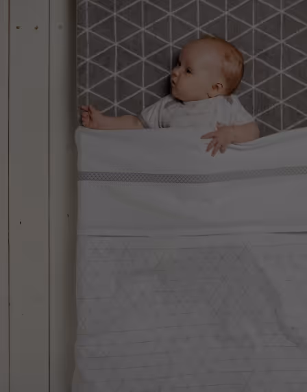 A thumbnail of the Alumio case study for b-boo baby & lifestyle GmbH, depicting a live picture of a baby sleeping on a checkered mattress, sticking out of a white blanket. 