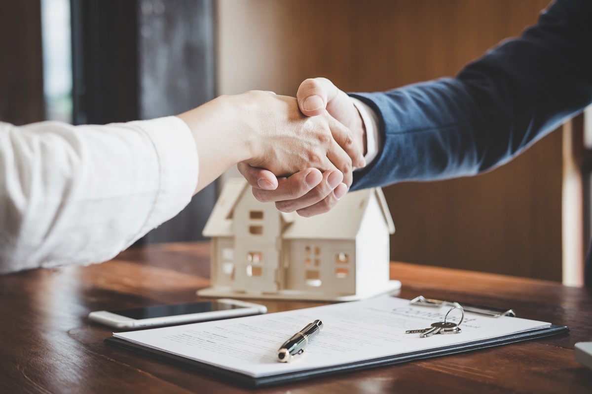 Two men shaking hands over a title form and a model house.
