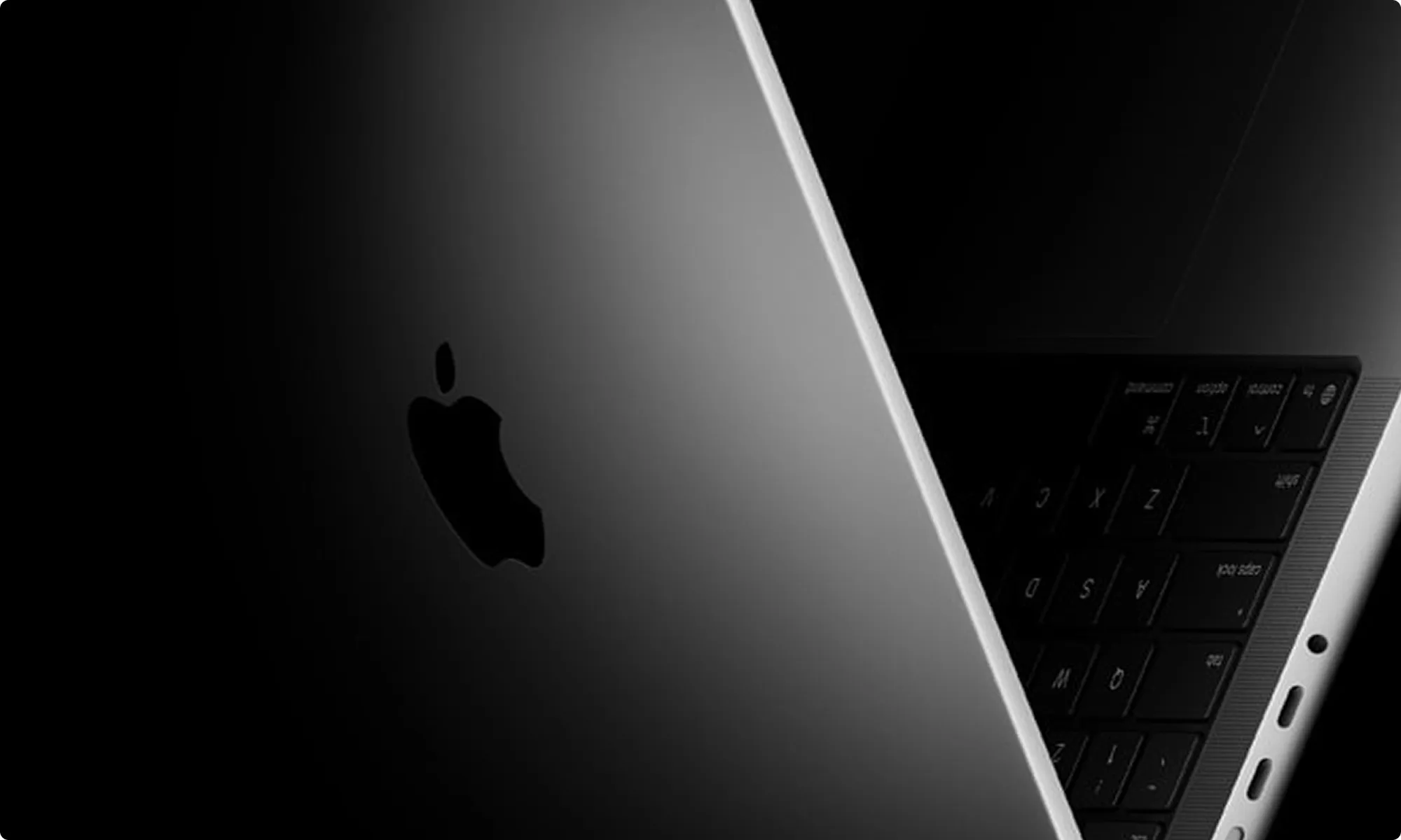 Close-up of a partially open Apple laptop showing the Apple logo and part of the keyboard in low light.