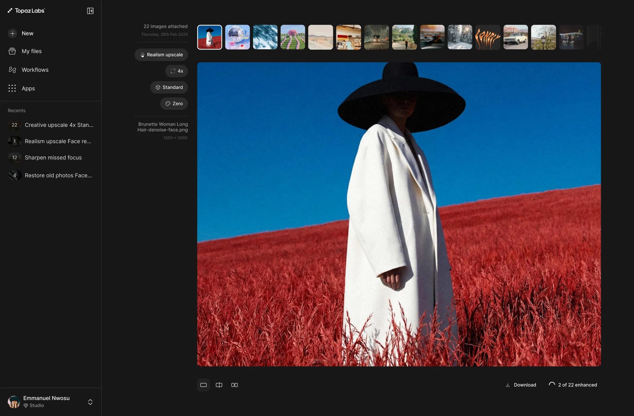 Woman in a white coat and wide-brimmed black hat standing in a red field under a clear blue sky.