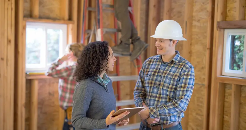 A man and woman talk on a construction site, collaborating on details for the Simply Home initiative.
