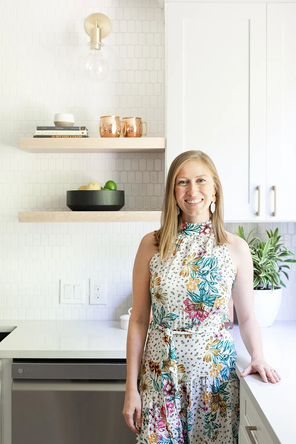 Blond women in a floral dress standing in a kitchen with white cabinets