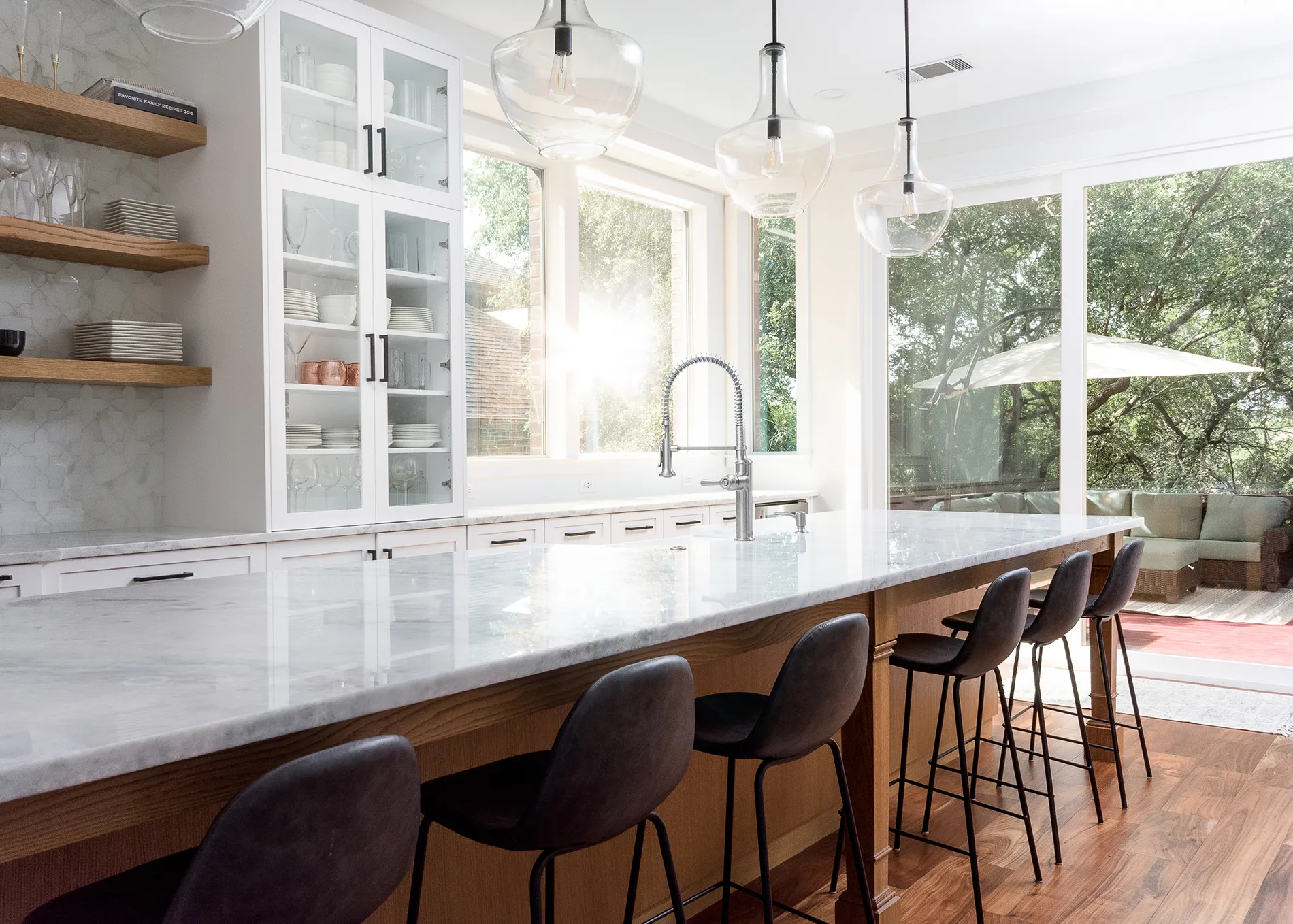 Kitchen with a large island with leather barstools, wood floors, white cabinets, and natural lighting