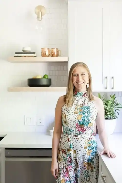 Blond women in a floral dress standing in a kitchen with white cabinets