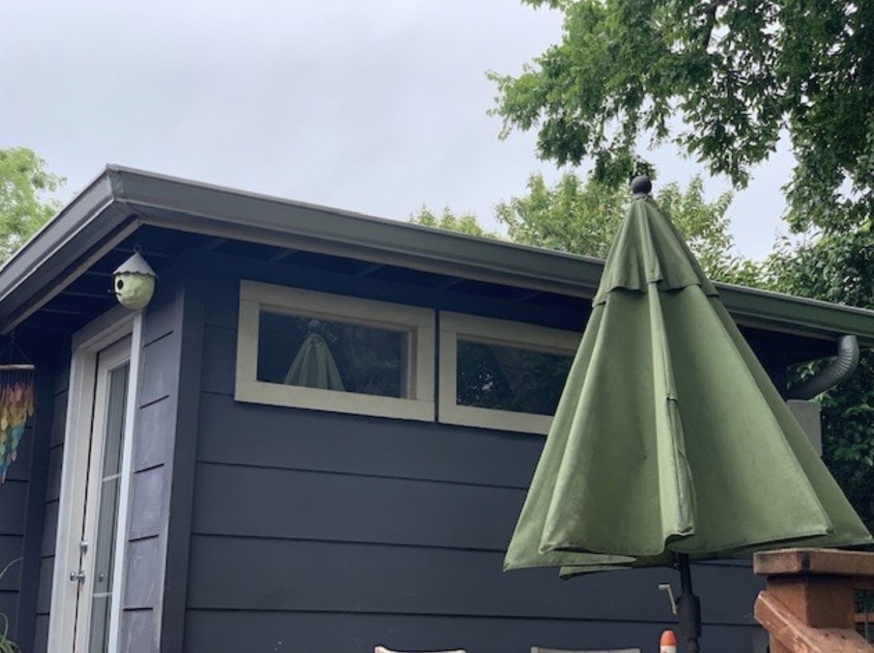 Corner of a small blue home and green patio table umbrella