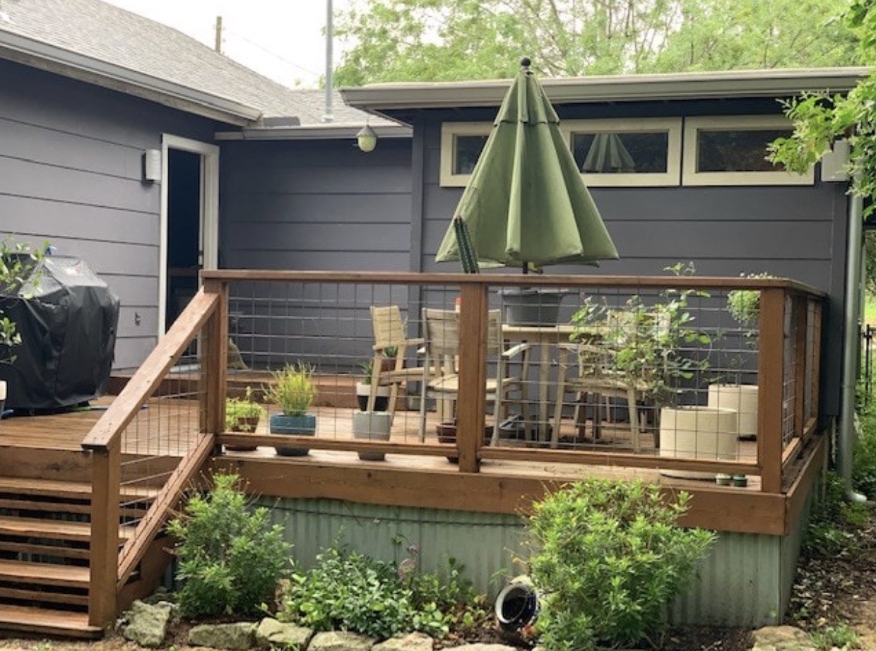 Backyard view of a wooden patio with a table and large green umbrella
