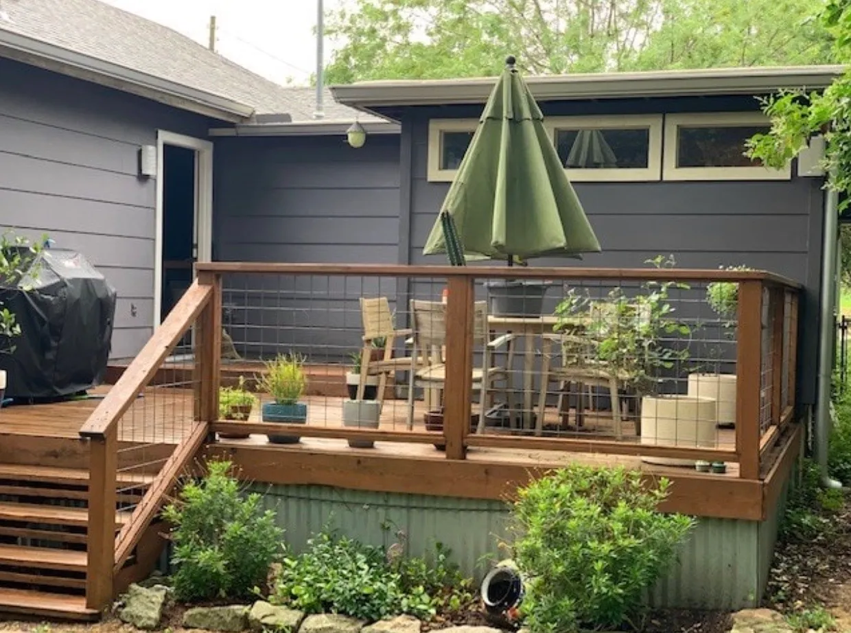 Backyard view of a wooden patio with a table and large green umbrella
