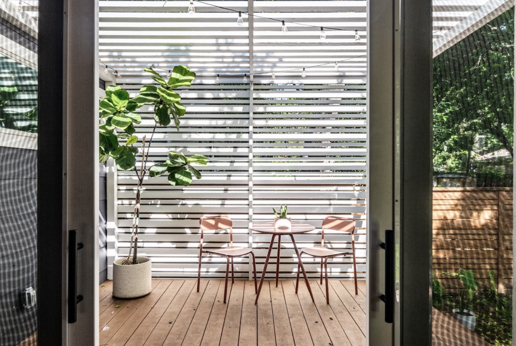 View of patio with a table and white slatted shade looking from inside the the house 