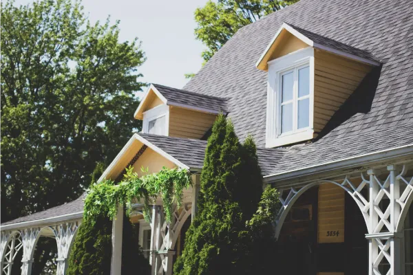 Yellow farm style house with tall evergreen bushes