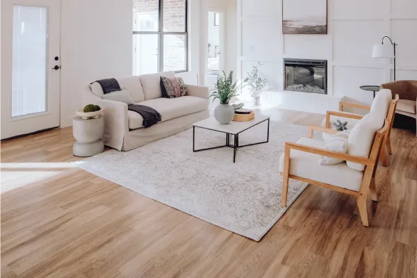Living room with a couch, two chairs, coffee table, a light area rug and wood floors