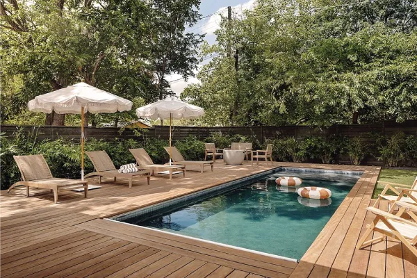 Backyard pool with wood flooring, lounge chairs and white umbrellas