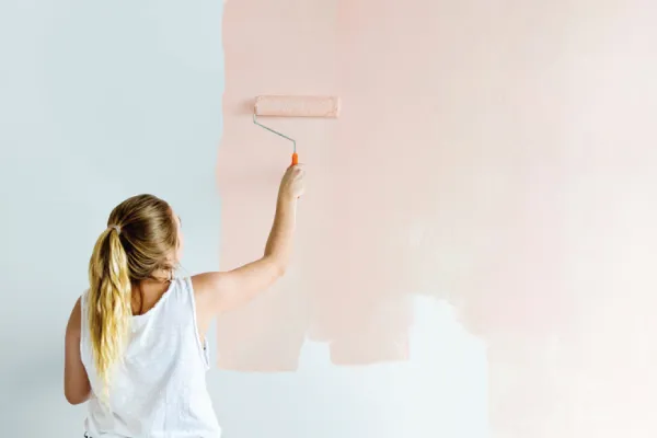 blonde women painting a grey wall light pink