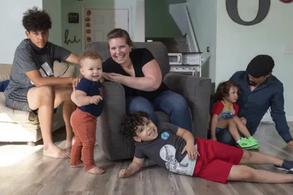 Family with four children sitting around a chair in a living room