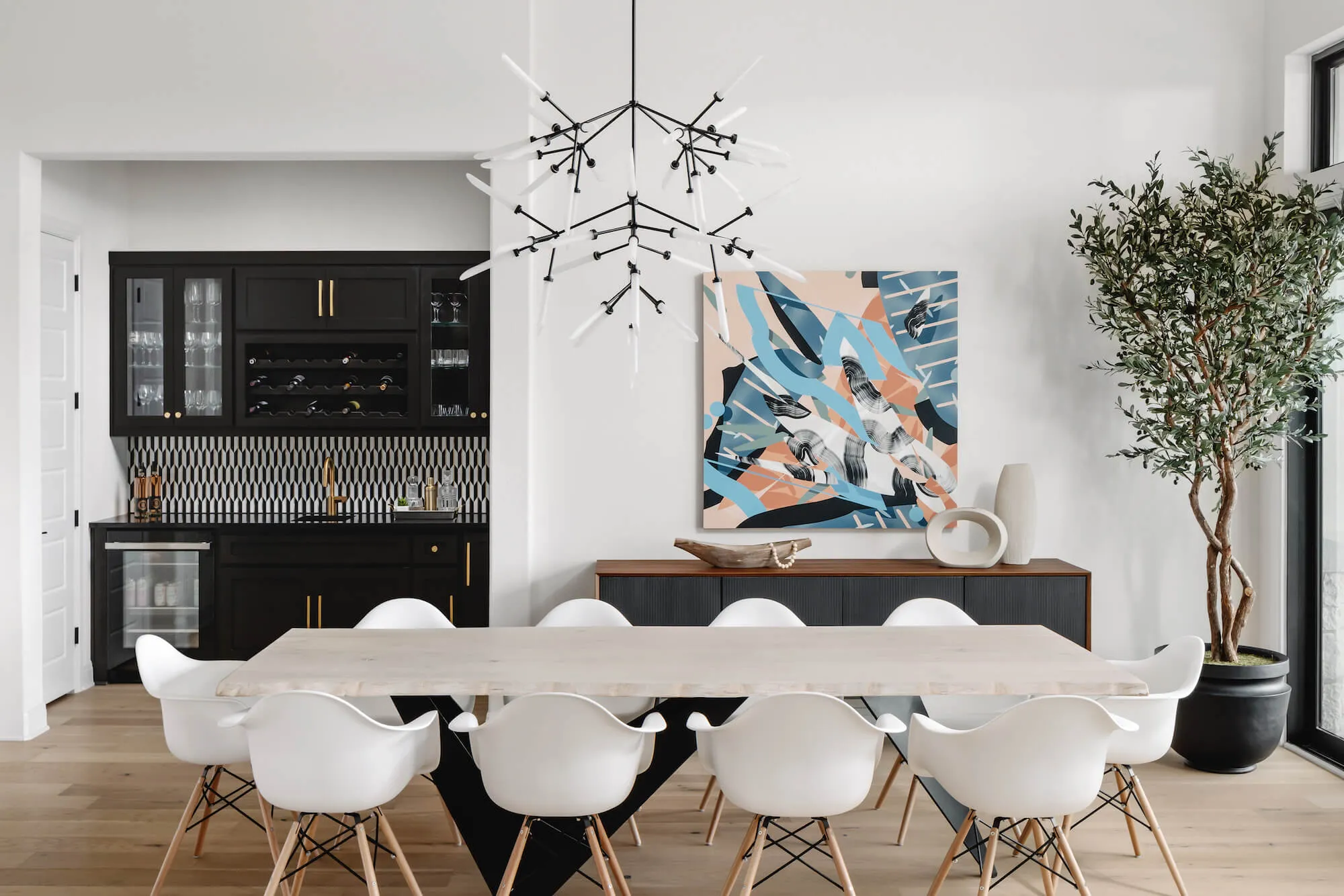 Dining room with a large ten person table with white chairs, wood floors, and a wet bar in the background