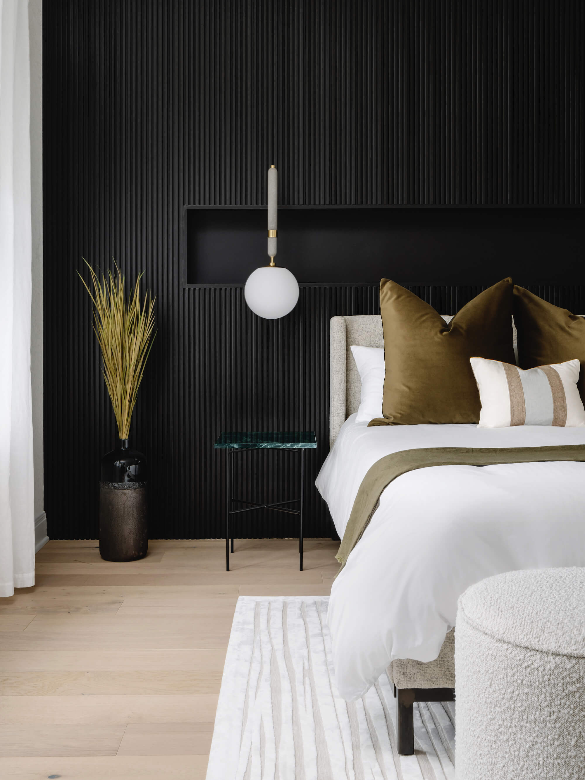 Bedroom with a black wall, bed with white bedding and green pillows, wood floors, and hanging bedside lighting