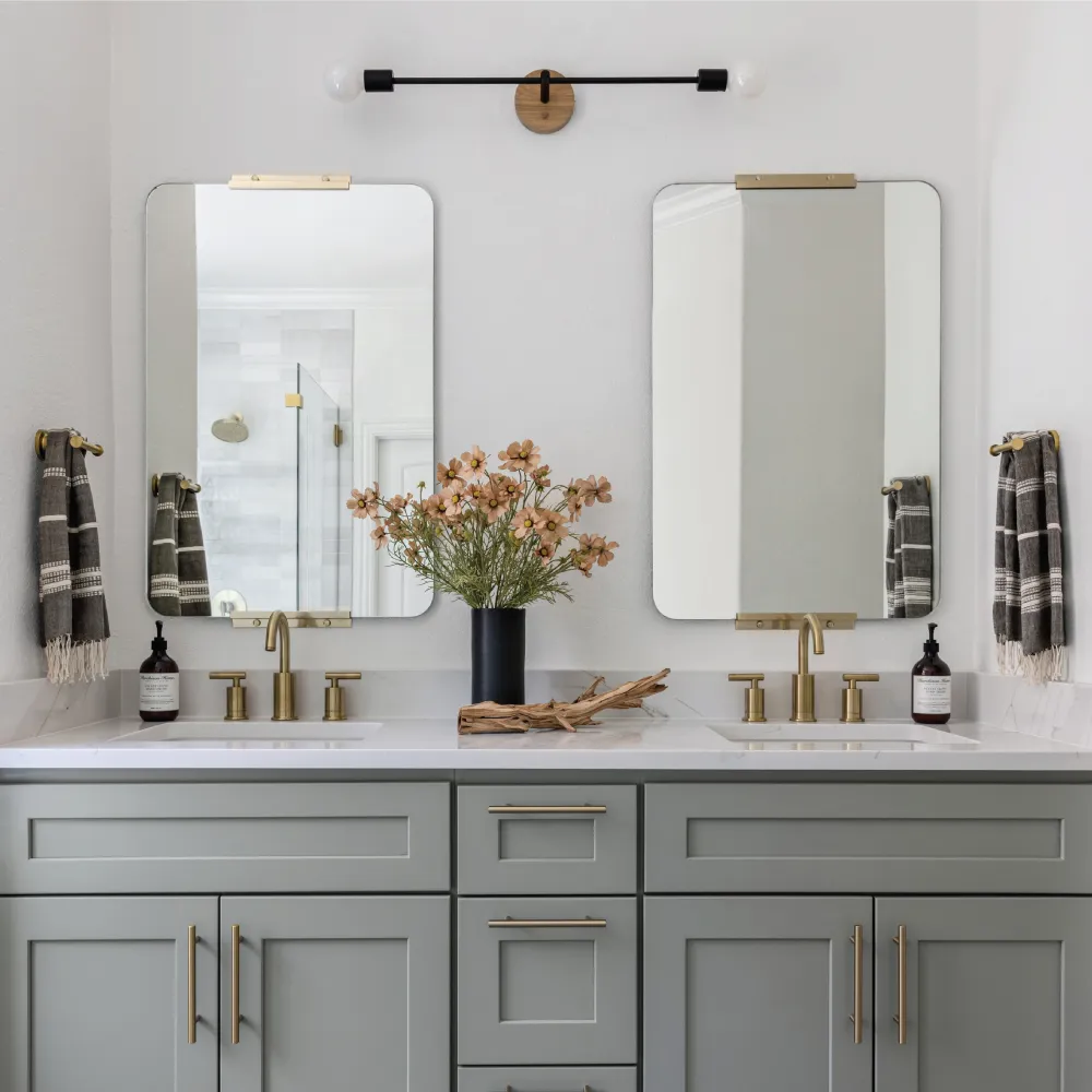 Bathroom with double sinks, sage cabinets, and two mirrors