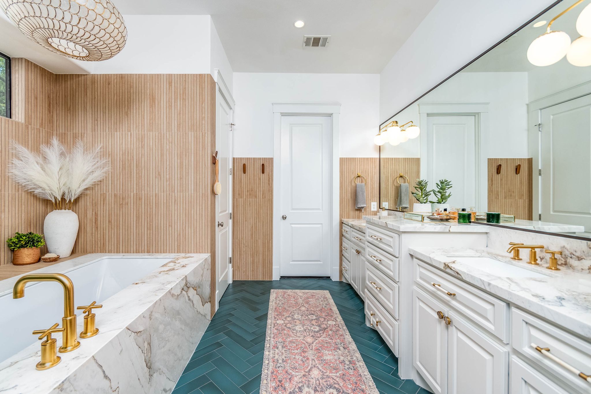 Bathroom with teal flooring, two sings with light grey cabinets, a large tub encased in marble and wood walls 