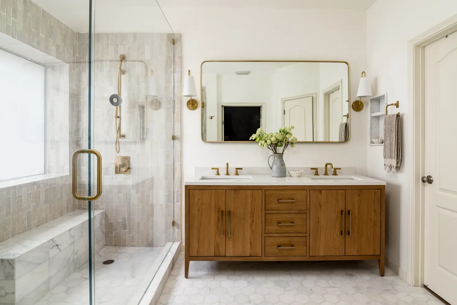 Modern double vanity, large mirror, and glass shower with marble bench.