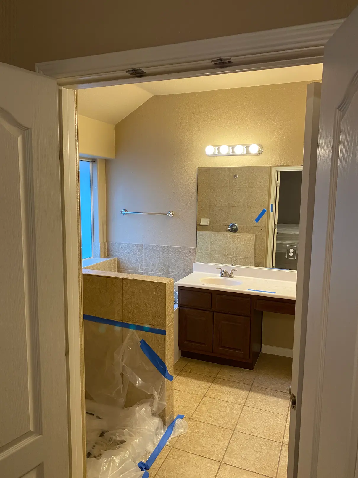 Renovated bathroom with brown tile, wood vanity, and a plastic-covered bathtub.