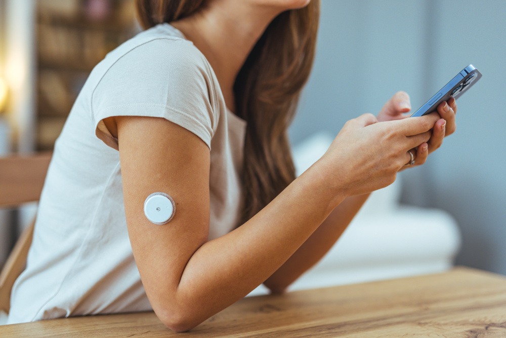 woman with glucose monitor on her arm, holding phone. 