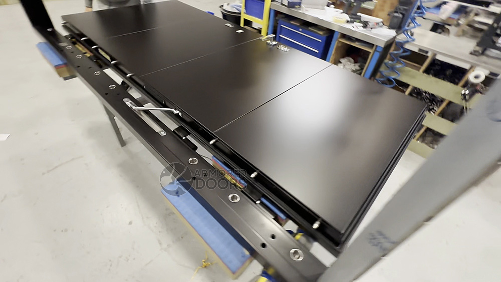 Minimalist steel security door being assembled with multi-point locking bolts and precision frame — in production at Armored Doors factory.