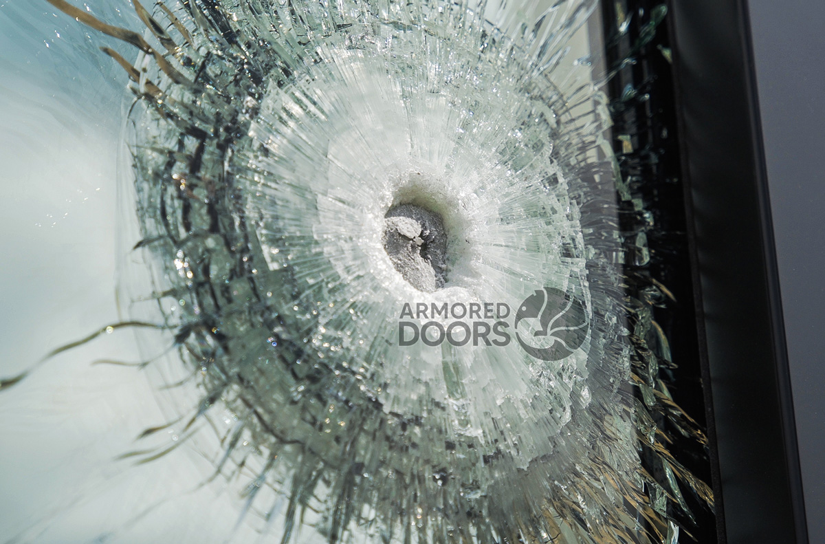Close-up of laminated ballistic security glass after AR-15 shooting test, showing impact resistance by Armored Doors.