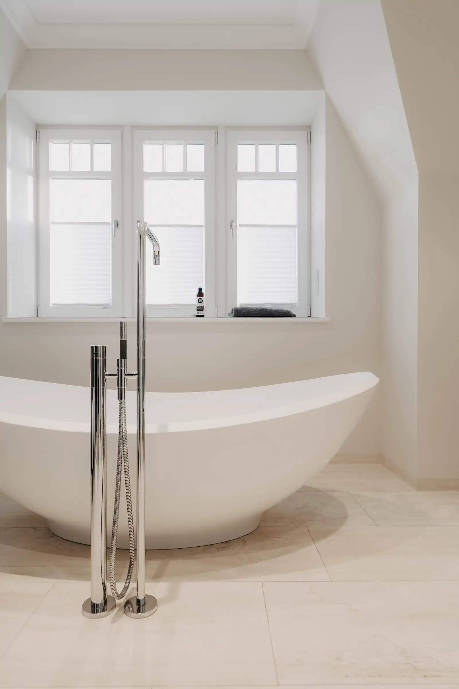 Weiße freistehende Badewanne mit Chrom-Armatur unter Dreifachfenster im Dachgeschoss – Engel & Völkers Villa